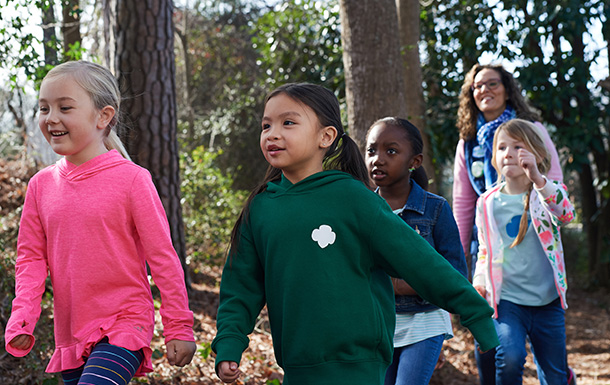 two young girl scouts outside at state park using binoculars - older girl is helping daisy girl scout see nature