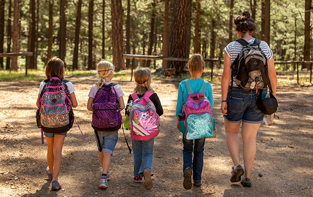 two young girl scouts outside at state park using binoculars - older girl is helping daisy girl scout see nature