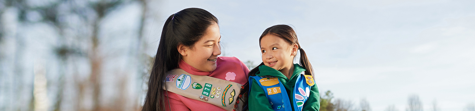  high school girl in senior ambassador sash smiling at daisy in vest uniforms with pins and badges displayed 