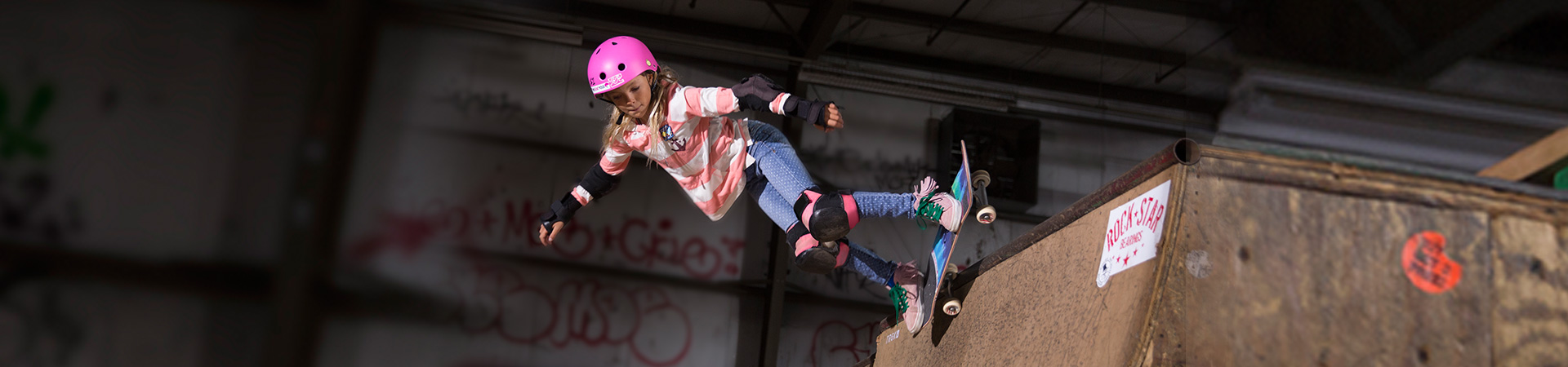  young girl on skateboard at top of ramp with pink helmet elbow and knee pads 
